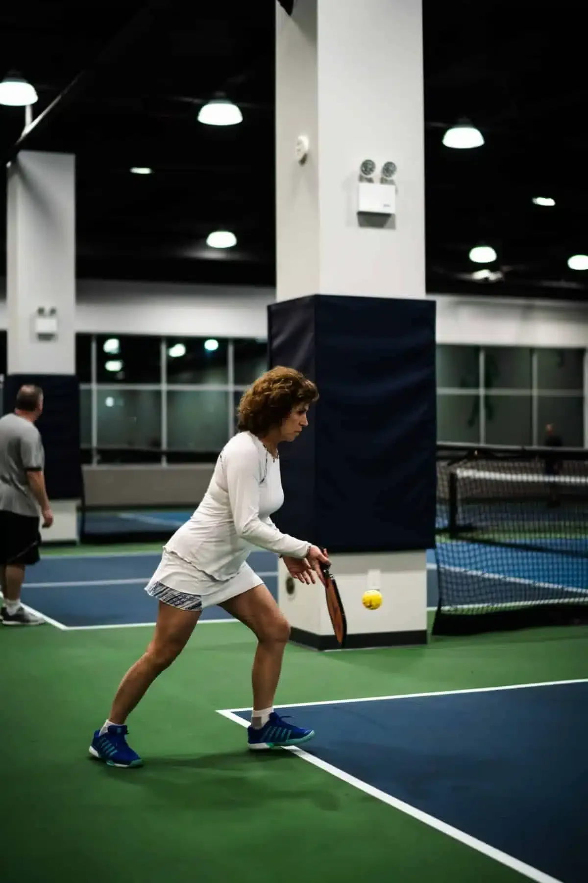 A player mid-shot on an indoor pickleball court